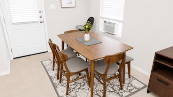 A dining area with a wooden table and chairs, a small plant on the table, and a patterned rug on the floor.
