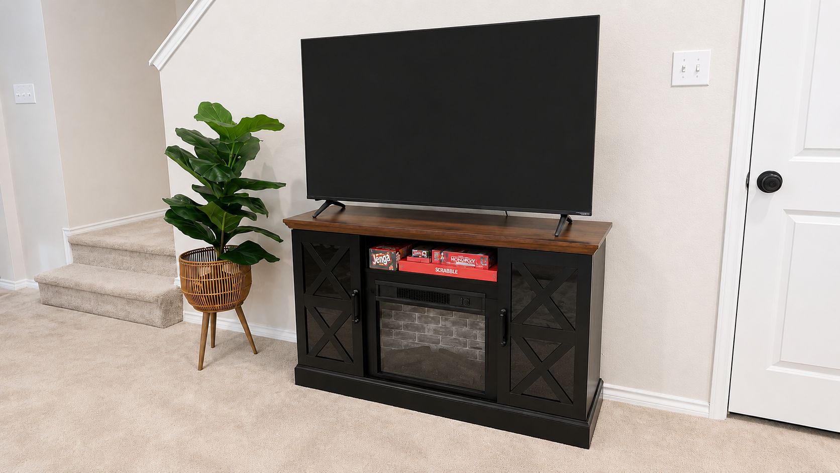 A black entertainment unit with a flat-screen TV, a plant, and storage boxes.