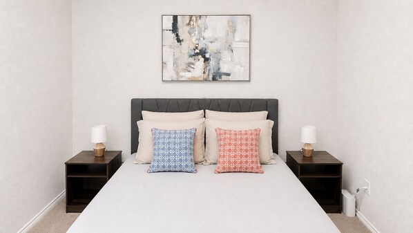 A bedroom with a bed, two nightstands, and a wall-mounted abstract painting.