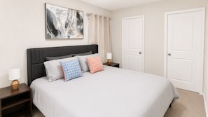 A bedroom with a bed, two nightstands, a lamp, a painting, and two doors.
