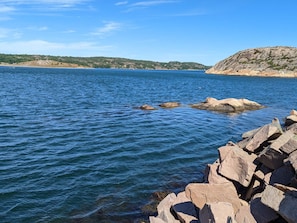 Eine Küstenlandschaft mit klarem, blauem Wasser, Felsformationen und einem fernen Hügel mit spärlicher Vegetation.