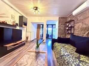 A living room with a flat-screen TV, a sofa, a coffee table, and a potted plant.