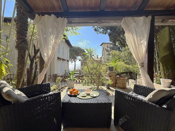 A covered outdoor seating area with wicker furniture and a table set with fruits and a teapot.