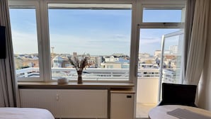 A hotel room with a large window, a bed, a small table, and a radiator. - Seeluft - Modern 1-room apartment with balcony and sea view, parking space, WLAN. (Sylt)