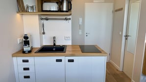 A compact kitchen with a sink, a coffee machine, and a kettle on the countertop. - Seeluft - Modern 1-room apartment with balcony and sea view, parking space, WLAN. (Sylt)