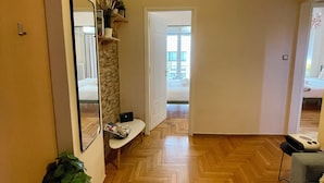 A hallway with a wooden herringbone floor, a mirror on the left, a bench with a basket, and a plant.