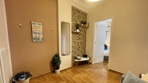 A spacious living area with a herringbone wooden floor, a grey sofa, a small side table, a potted plant, and a mirror on the wall.