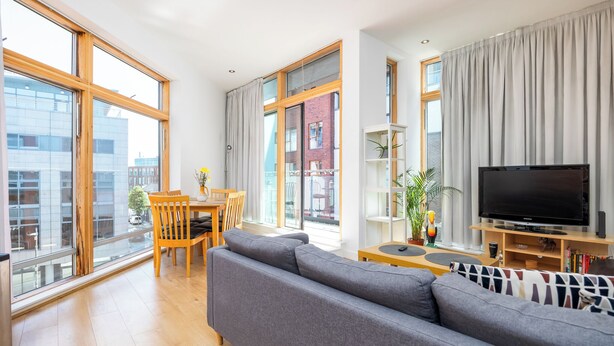 A modern living room with a grey sofa, wooden dining table, and a flat-screen TV. - 3 Bed in Dublin city centre 10min to Spire (Dublin 1)