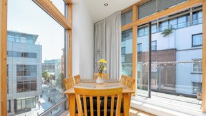 A dining area with a wooden table and chairs, a vase with flowers, and large windows offering views of buildings and a street. - 3 Bed in Dublin city centre 10min to Spire (Dublin 1)