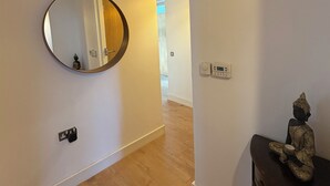 A hallway with a wooden floor, a round mirror on the left, a statue on a table to the right, and a light switch on the wall. - 3 Bed in Dublin city centre 10min to Spire (Dublin 1)