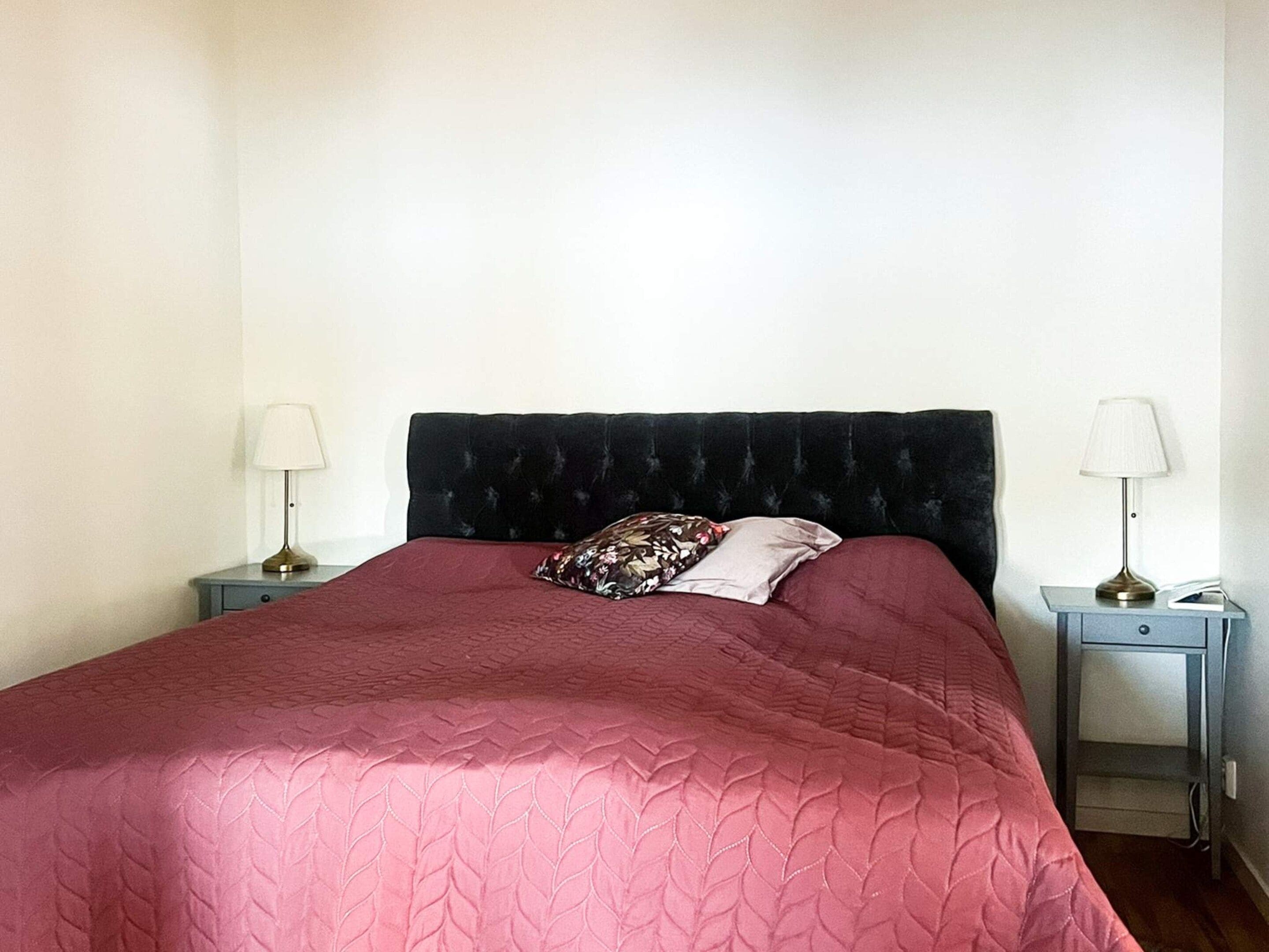 A single bed with a dark headboard, two bedside tables with lamps, and a red bedspread.