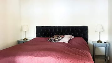 A single bed with a dark headboard, two bedside tables with lamps, and a red bedspread.