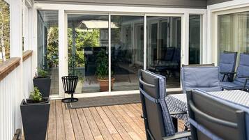 A covered patio with a wooden deck, outdoor furniture, and sliding glass doors leading to an interior space.