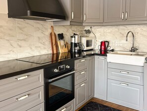 A modern kitchen with grey cabinets, a black countertop, a stainless steel range hood, a microwave, a kettle, and a sink. - 5 Star Holiday Home in Eksjo (Eksjo)