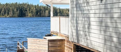 A waterfront property with a wooden deck, a covered outdoor area, and a view of the water and forest.