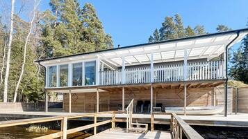 A modern house with a glass conservatory, wooden deck, and a dock extending into a body of water.