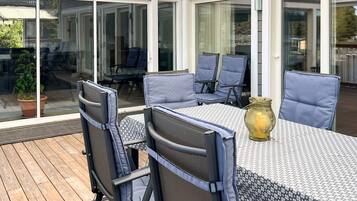 An outdoor patio with a table and chairs, a potted plant, and a glass door leading to a covered area.