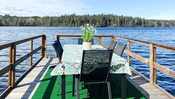 A wooden deck with a table and chairs, a potted plant, and a view of a lake and forest.