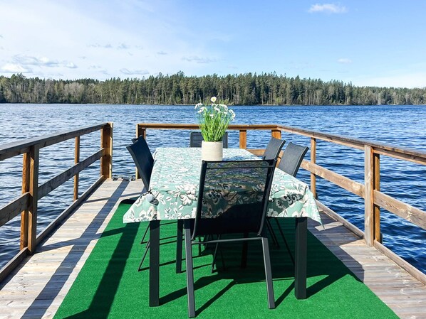 A wooden deck with a table and chairs, a potted plant, and a view of a lake and forest.