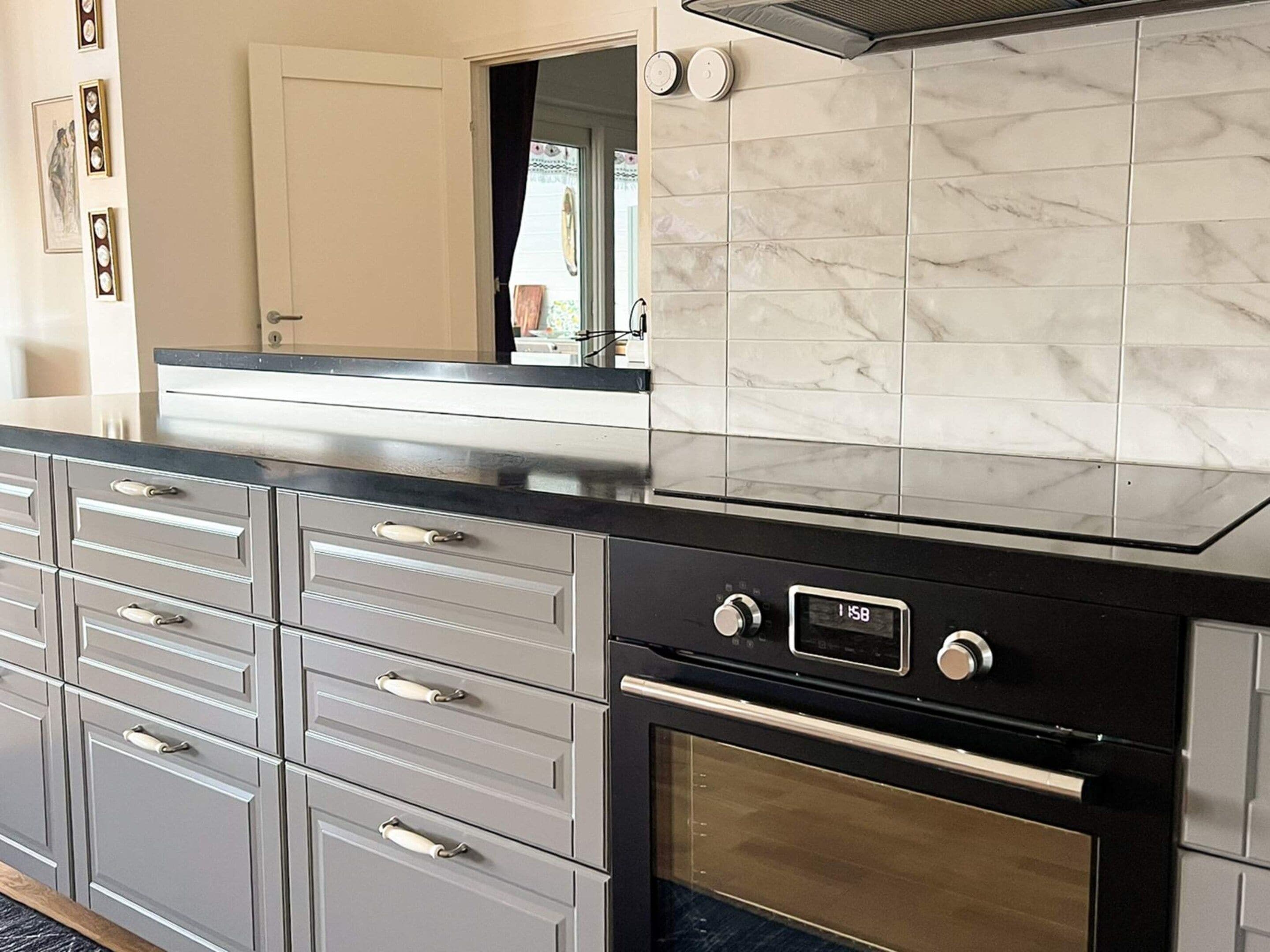 A kitchen with a black oven, a digital clock, and a marble backsplash.