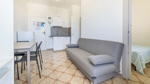 Un espace de vie compact comprenant un coin cuisine, un canapé, une table à manger avec des chaises et un lit avec une couverture à rayures.