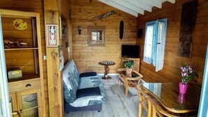 A cozy cabin interior with a sofa, wooden dining table, and a television. - CHALET JAUNE, a 2300m2 park, wifi, parking, swimming pool, kitchen, happiness (Saint-Pierre)