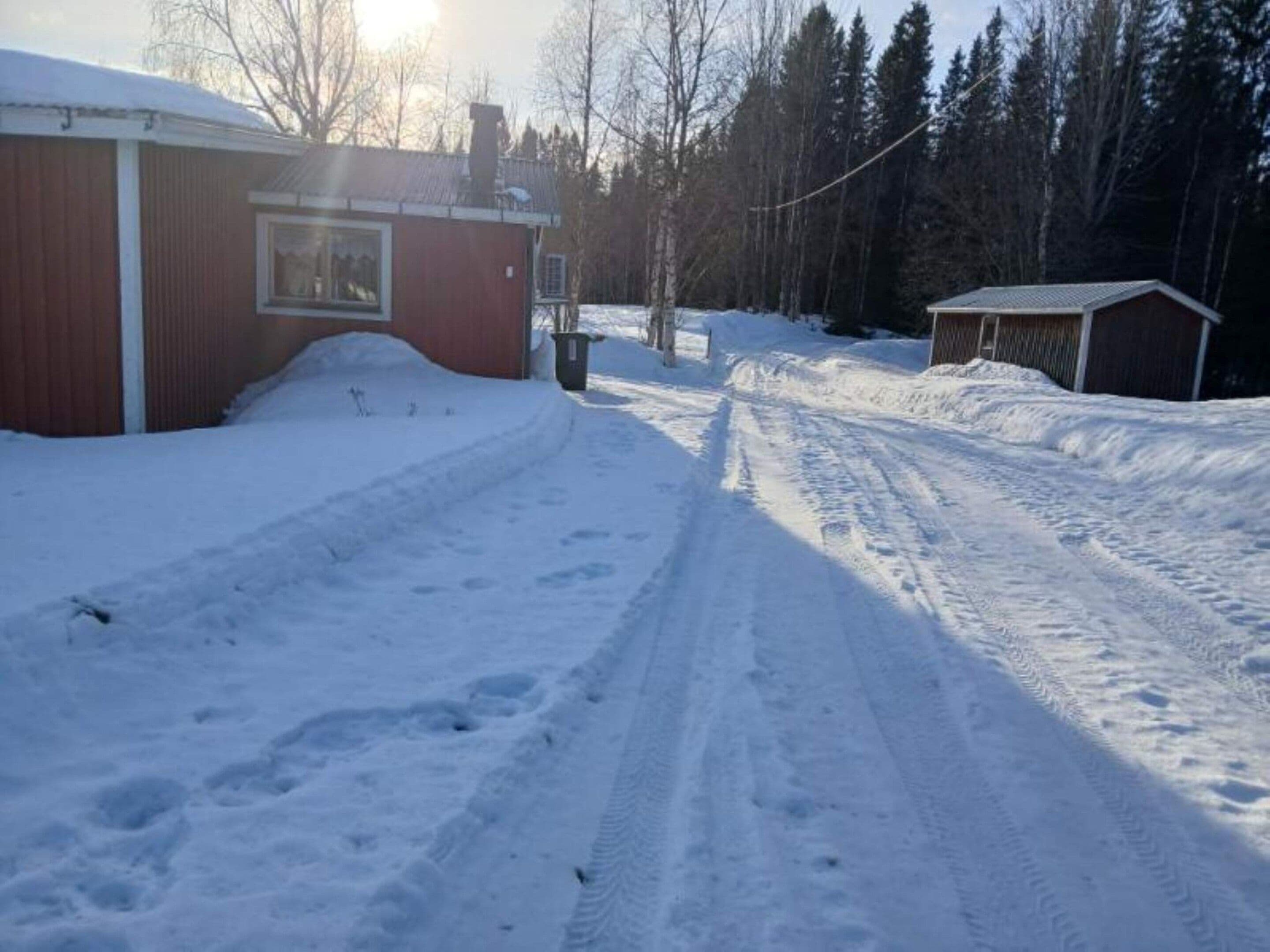 Un sendero cubierto de nieve que lleva a un edificio de fachada roja y una ventana.