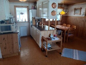 A compact kitchen with a microwave, refrigerator, and wooden cabinets. There's a dining area with a table and chairs, and a small shelf with books. - 5 Person Holiday Home in Lidsjoberg (Lidsjöberg)