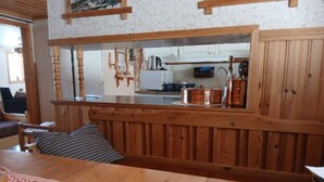 A wooden dining table with a patterned runner, a bench, and a view into a kitchen area with copper cookware. - 5 Person Holiday Home in Lidsjoberg (Lidsjöberg)