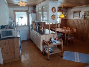 Kompakti keittiö, jossa on puiset kaapit, mikroaaltouuni sekä ruokailutila, jossa on pöytä ja tuolit.