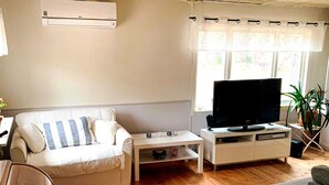 A living room with a white sofa, a TV on a white stand, a small table, and a window with curtains. - 8 Person Holiday Home in Arla (Arla)