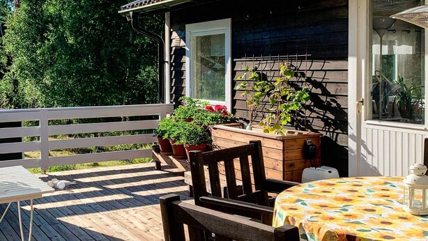 A wooden deck with a table and chairs, potted plants, and a staircase leading to a building. - 8 Person Holiday Home in Arla (Arla)