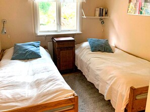 A bedroom with two single beds, a small wooden cabinet, a window with a view of greenery, and a shelf with books. - 8 Person Holiday Home in Arla (Arla)