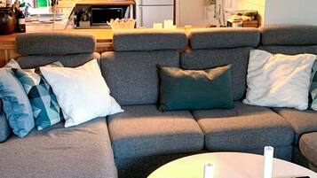 A grey sofa with multiple cushions, a white coffee table with candles, and a kitchen area in the background.