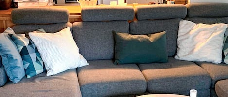A grey sofa with multiple cushions, a white coffee table with candles, and a kitchen area in the background.