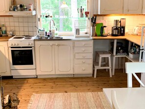 A kitchen with white cabinets, a stove, a sink, and a window with a view of trees. - 8 Person Holiday Home in Arla (Arla)