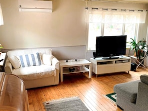 A living room with a sofa, a coffee table, a television on a stand, and a window with curtains. - 8 Person Holiday Home in Arla (Arla)