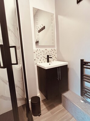A modern bathroom with a white sink, dark cabinets, a tiled backsplash, and a black trash can. - Stylish 5-Bed Home, Off-Street Parking, for families, groups, or business stays (Kidderminster)
