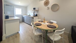 A compact kitchen with a dining area, white cabinets, a microwave, and a small dining table set for four. - Charming House with garden, close to the beach - Aircond & Parking (Palavas-les-Flots)