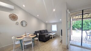 A modern living room with a dining area, a sofa, a TV, and a large sliding glass door leading to an outdoor patio. - Charming House with garden, close to the beach - Aircond & Parking (Palavas-les-Flots)