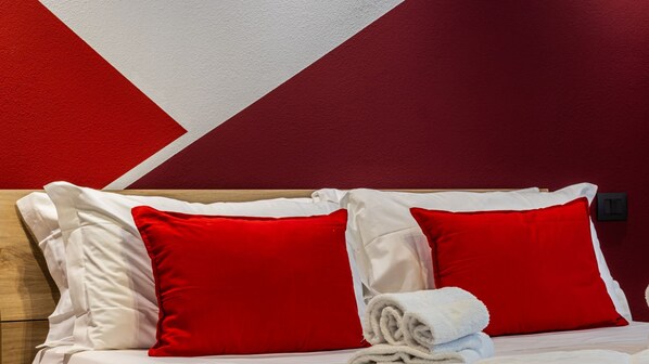 A bed with white and red bedding, a wooden headboard, and a red and white geometric wall design.