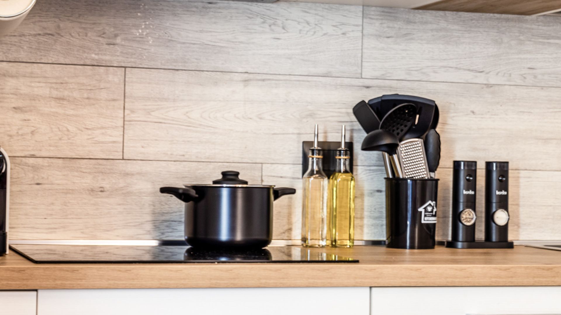 Un plan de travail de cuisine avec une casserole noire, deux bouteilles d’huile, un ensemble d’ustensiles de cuisine et deux appareils électroménagers noirs.