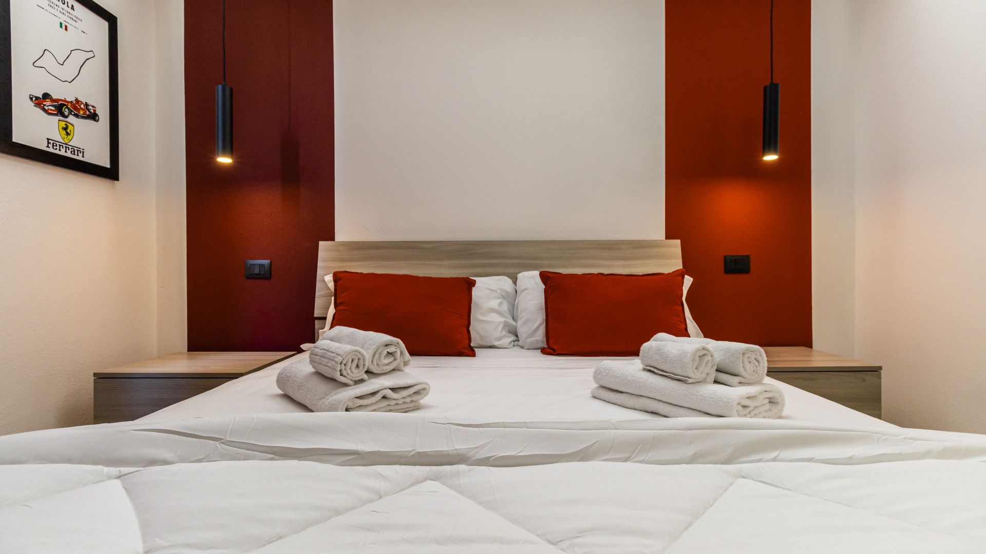Une chambre d’hôtel avec un grand lit, deux oreillers rouges, une tête de lit et deux tables de chevet avec des lampes.