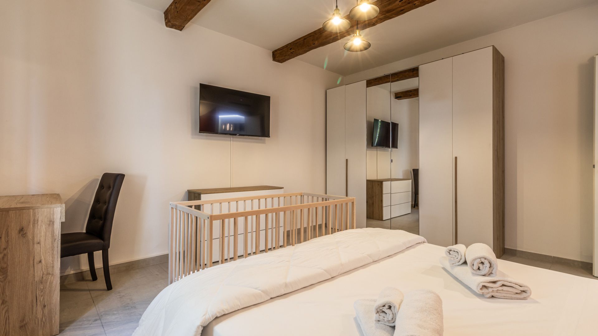 Een slaapkamer met een bed, een ledikant, een aan de muur bevestigde televisie en een spiegel.