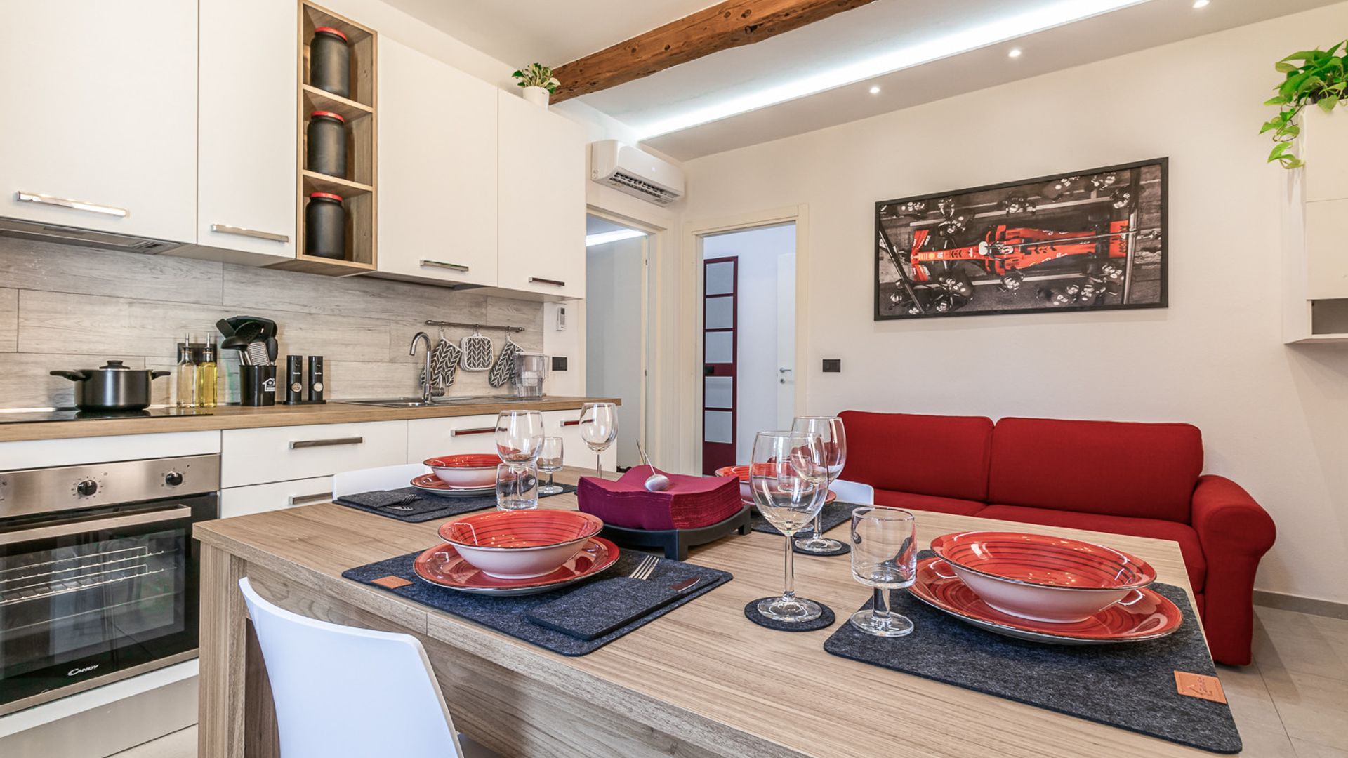 Une cuisine moderne avec des meubles en bois, une table à manger pour quatre personnes et un canapé rouge dans l’espace repas.