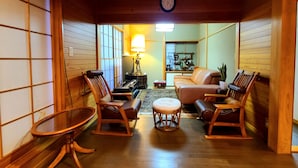 A traditional Japanese-style living room with tatami flooring, a low wooden ceiling, and a view into the kitchen area. - Maple House - Kawaguchiko Otsuki - 10 people or more (大月市)