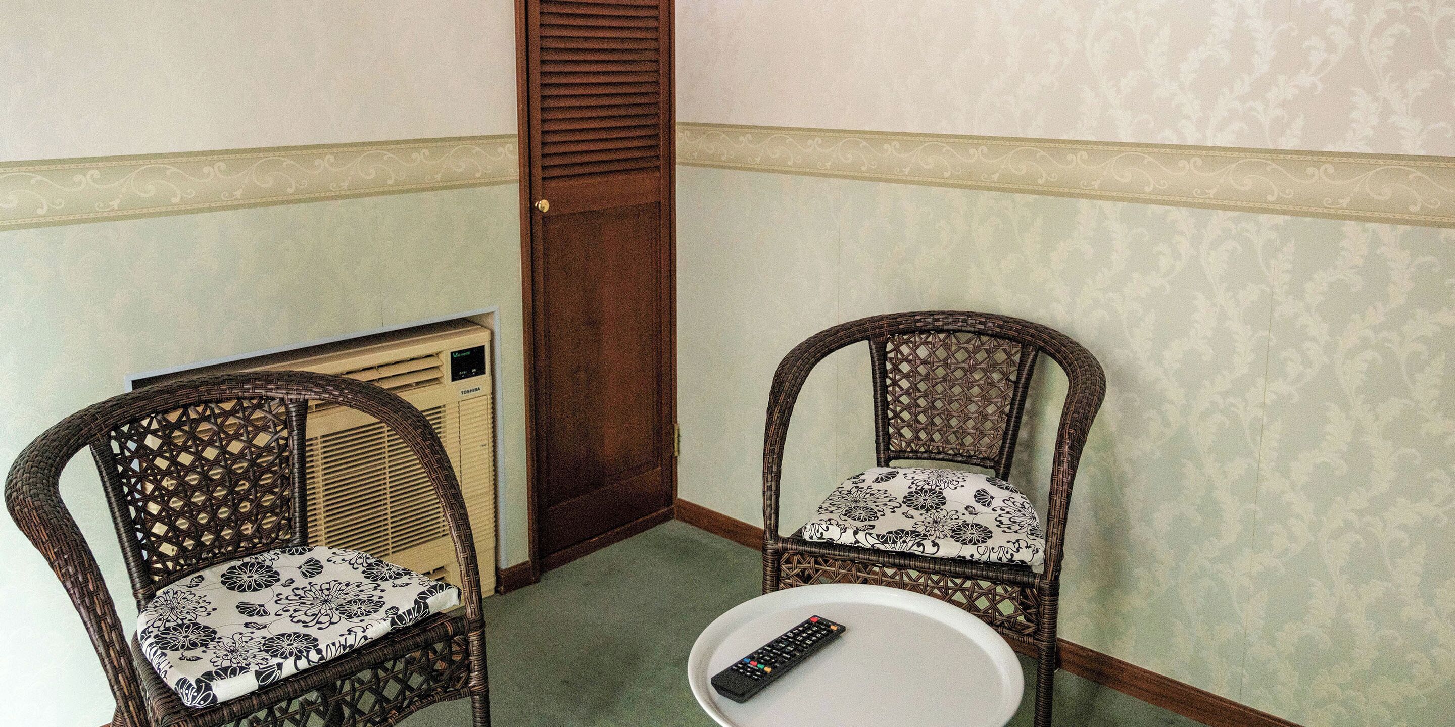 Two wicker chairs with floral cushions, a small round table, and a remote control on the table.