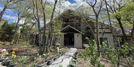 A two-story house with a stone facade, a wooden deck, and a garden with potted plants and flowers.