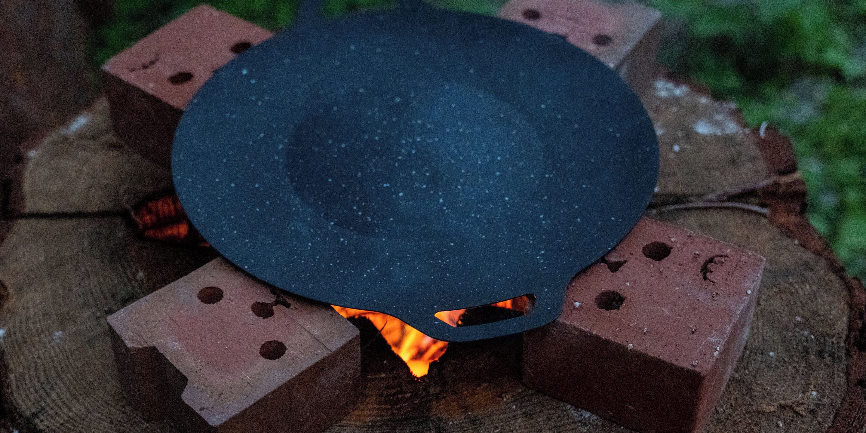 A black pot on a brick stove with visible flames underneath.