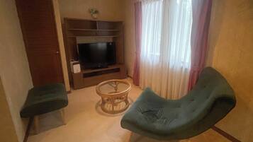 Uma sala de estar com televisão, uma mesa de centro redonda e duas cadeiras.